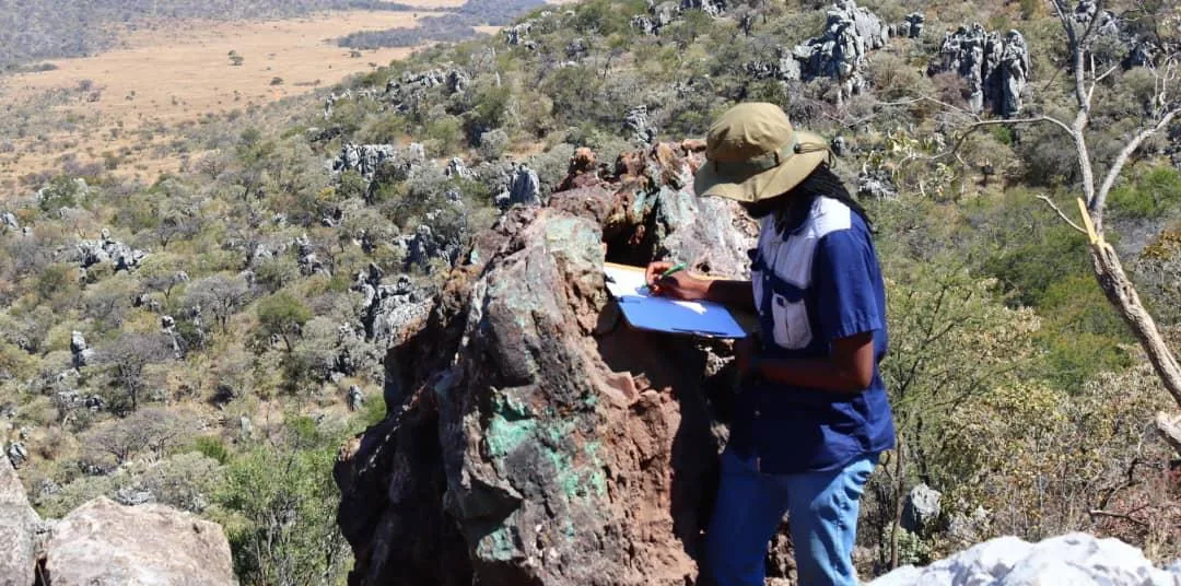 Geologist recording observations at a copper-stained gossan outcrop